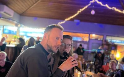 Twee collega's zingen karaoke onder feestverlichting tijdens een eindejaarsfeest
