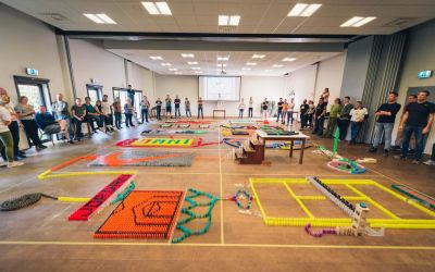 Grote groep collega's rond een gezamenlijk domino-parcours tijdens een kick-off