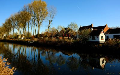 Herfstbomen en huizen weerspiegeld in de vaart van Damme