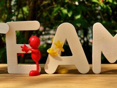 Wooden letters spelling TEAM, with small figures holding them up together