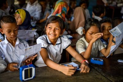 Smiling schoolchildren holding the Solar Buddy lights that teams assemble during the team building