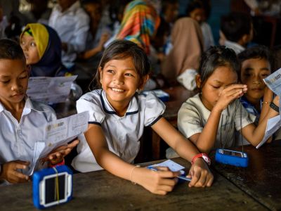Smiling schoolchildren holding the Solar Buddy lights that teams assemble during the team building